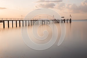 Long exposure view of a pier on a lake at sunset, with beautiful