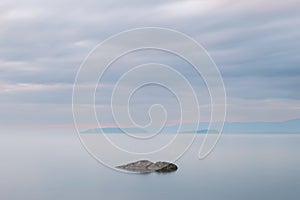 Long exposure view of a rock in Trasimeno lake Umbria, with islands in the background and moody sky