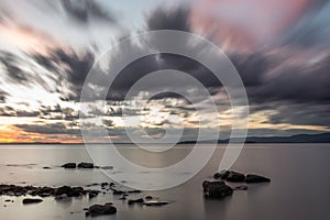 Long exposure view of rocks in Trasimeno lake Umbria, with moving clouds at dusk