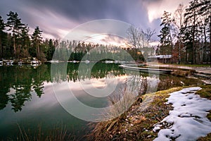 Long-exposure view of trees and a cottage on the coasts of a lake on a cloudy autumn day