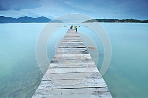 Long exposure of wooden jetty at sea facing island with cloud an