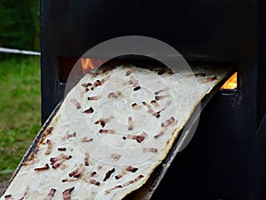 Long Flammekueche: Close-up Cooking of Alsace's Flammkuchen with Flame, a Delicious Mix of Bacon, Cream, and Onions