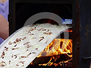 Long Flammekueche: Close-up Cooking of Alsace's Flammkuchen with Flame, a Delicious Mix of Bacon, Cream, and Onions