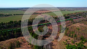 A long freight train with green train car wagons travels among the forest.