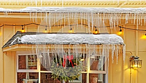 long frozen icicles hanging and dripping from upper and lower roof ledges with snow