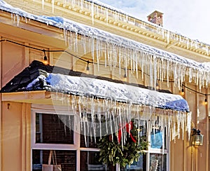 long frozen icicles hanging and dripping from upper and lower roof ledges with snow