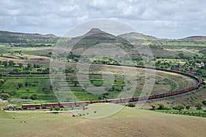 Long goods freight train passing through a big curve in hilly railway line with monsoon clouds hovering over , at Daundaj,