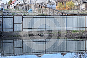 long gray metal fence wall with a closed door on the shore near the water