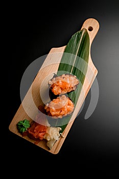 Long green leaf on a wooden board with sushi set on a black background