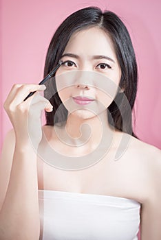 Long hair asian young beautiful woman applying cosmetic powder brush on smooth face isolated over pink background. natural makeup.