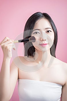 Long hair asian young beautiful woman applying cosmetic powder brush on smooth face isolated over pink background. natural makeup.