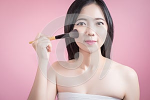 Long hair asian young beautiful woman applying cosmetic powder brush on smooth face over pink background. natural makeup.