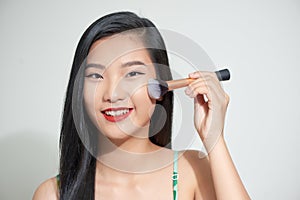 Long hair asian young beautiful woman smile and fun, touch her face and hold cosmetic powder brush set on white