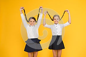 Long hair growth stimulant. Cute small children holding long hair braids on yellow background. Adorable little girl