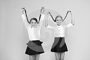 Long hair growth stimulant. Cute small children holding long hair braids on yellow background. Adorable little girl