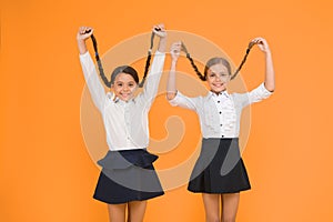 Long hair growth stimulant. Cute small children holding long hair braids on yellow background. Adorable little girl