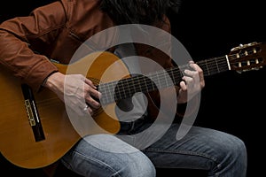 Long hair male guitarist playing with acoustic guitar in leather