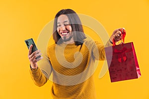 A long haired bearded happy young man hanging a phone and a red gift bag in his right hand inside a room