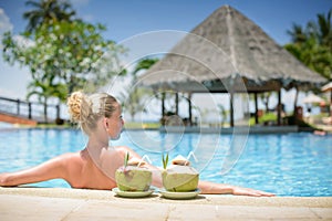 Long haired blonde woman with flower in hair in bikini on tropical pool