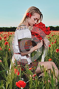 Long-haired blonde young woman in a white short dress on a field of green wheat and wild poppies