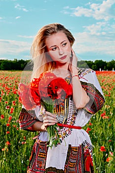 Long-haired blonde young woman in a white short dress on a field of green wheat and wild poppies