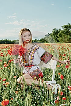 Long-haired blonde young woman in a white short dress on a field of green wheat and wild poppies