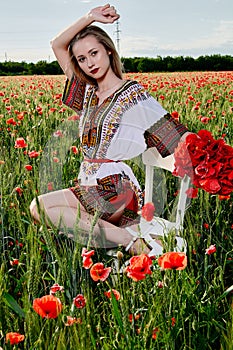 Long-haired blonde young woman in a white short dress on a field of green wheat and wild poppies