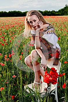 Long-haired blonde young woman in a white short dress on a field of green wheat and wild poppies