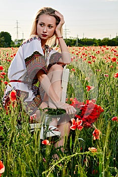 Long-haired blonde young woman in a white short dress on a field of green wheat and wild poppies