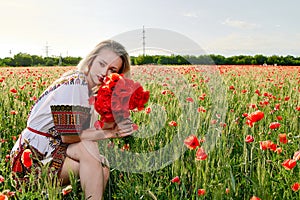 Long-haired blonde young woman in a white short dress on a field of green wheat and wild poppies