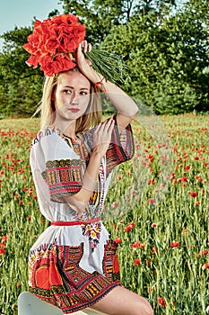 Long-haired blonde young woman in a white short dress on a field of green wheat and wild poppies