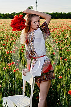 Long-haired blonde young woman in a white short dress on a field of green wheat and wild poppies