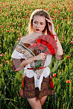 Long-haired blonde young woman in a white short dress on a field of green wheat and wild poppies