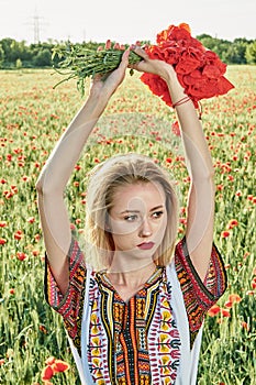 Long-haired blonde young woman in a white short dress on a field of green wheat and wild poppies