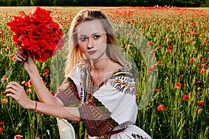 Long-haired blonde young woman in a white short dress on a field of green wheat and wild poppies