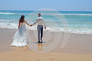 Long-haired brunette bride and groom in a suit. newlyweds holding hands, go to the sand in the water of the Indian Ocean