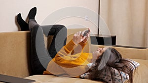 Long haired brunette in pullover on sofa types on smartphone