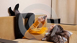 Long haired brunette in pullover on sofa types on smartphone