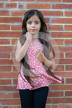 Long-haired Colombian girl adjusts her hair next to a brick wall