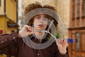 A long-haired curly-haired guy in a brown shirt uses a metal comb. Emotions before a haircut in a hairdresser