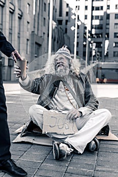 Long-haired dirty man sitting on cold ground with cardboard nameplate