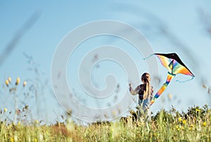 Long-haired Girl with flying a colorful kite on the high grass meadow in the mountain fields. Happy childhood moments or outdoor