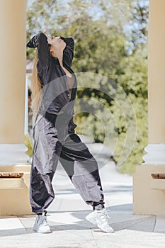 Long-haired girl in street corduroy clothes stands in a pose between the columns in the park