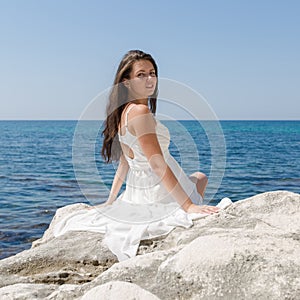 Long-haired girl in wedding dress sitting on stone