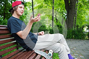Long-haired hipster skater in a cap sits on a bench and spins on a spin-spinner