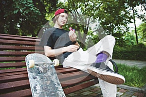 Long-haired hipster skater in a cap sits on a bench and spins on a spin-spinner