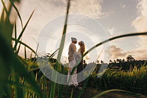 long haired man hugs his delicate curly woman in the lights of sunset