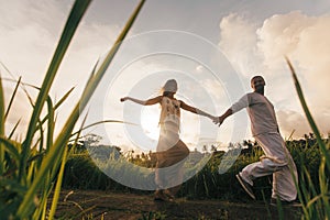 long haired man hugs his delicate curly woman in the lights of sunset