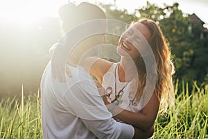 long haired man hugs his delicate curly woman in the lights of sunset
