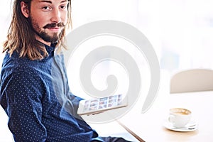 Long haired modern man with tablet sitting next to window